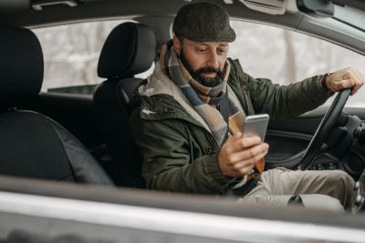 Distracted driving is even more dangerous in the winter: a man dressed for snow checks his mobile phone while behind the wheel
