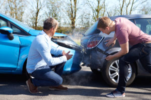 Two male drivers look at their bumper damage and steam or smoke after they get into an accident