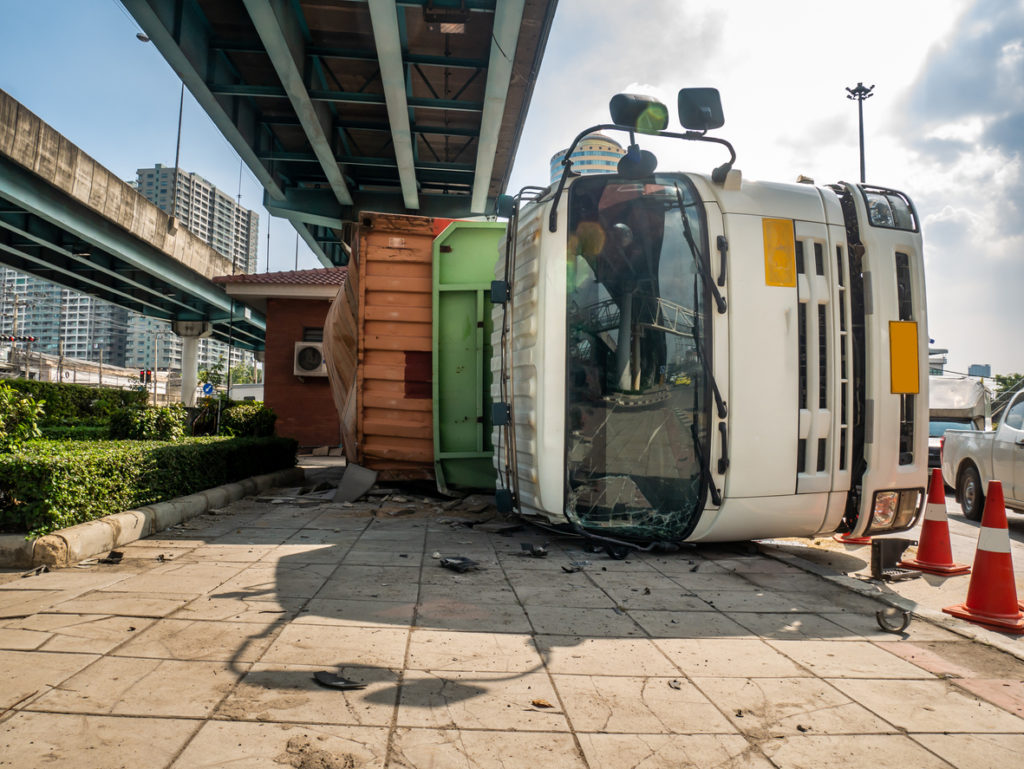 A truck that's overturned on its side under an overpass.