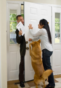 Resident tries to close the front door to her house as her dog barks and a door-to-door salesman steps into the doorway insisting that she sign a sales contract