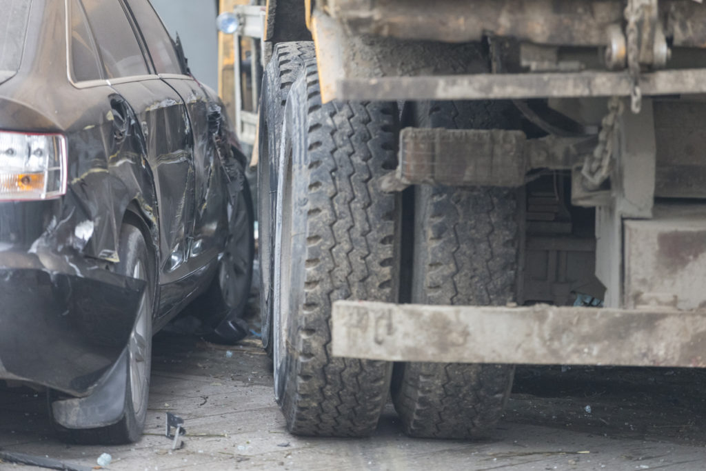 A dumptruck, or other construction-related heavy duty truck, jumped the curb and sideswiped a small sedan