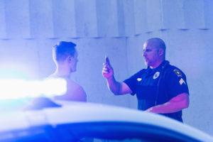 Police officer giving a sobriety test to a young man who he suspects is driving under the influence of drugs or alcohol