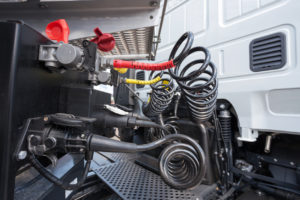 Closeup view of the area behind the cab of a commercial semitruck, where hoses and electrical cables are connected to the trailer