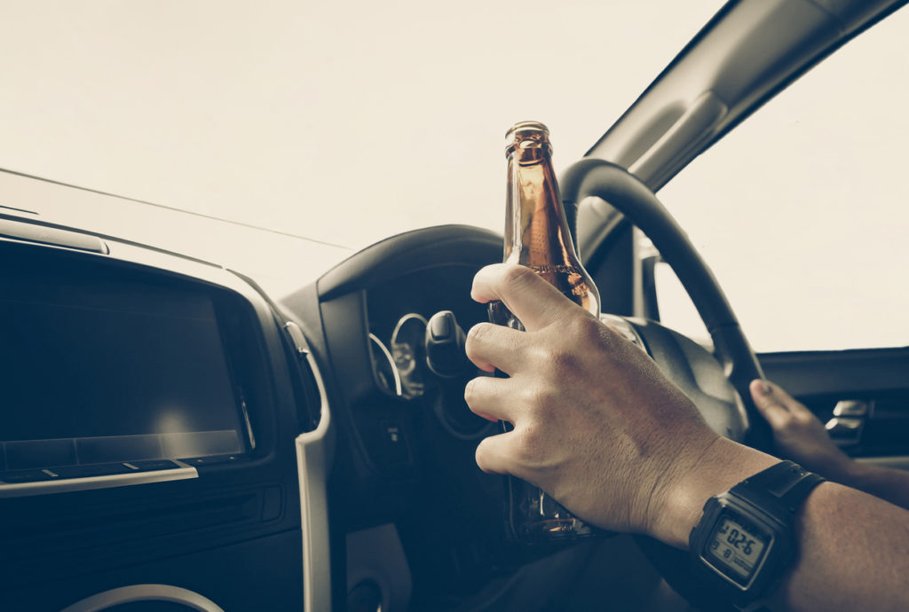 A drunk driver holding a beer by the wheel